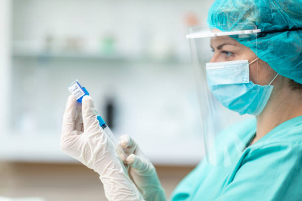 istock Female doctor in protective workwear pulling COVID-19 vaccine liquid from vial 1227138012
