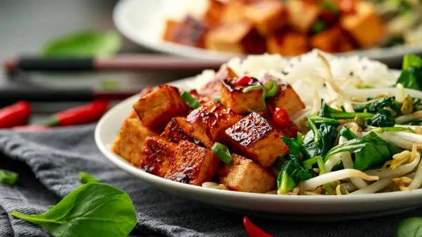 Fried Asian tofu in sweet chilli glaze served with rice, steamed spinach and beansprouts. Vegetable healthy food.