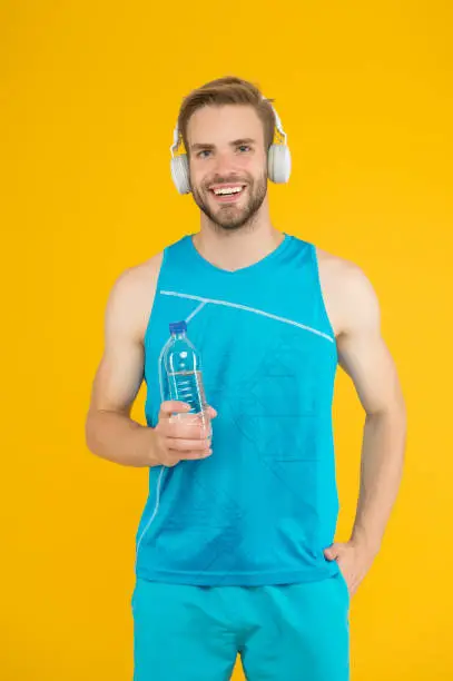 Photo of Keep body and mind in good shape. Happy sportsman hold water bottle. Fitness trainer. Feeling thirst. Thirst and dehydration. Thirst control. Drinking water. Cheerful athletic guy listening music