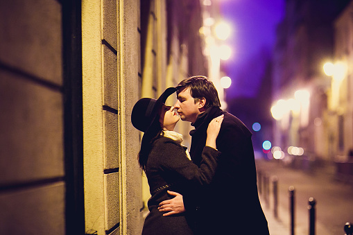 girl in hat and a man kiss and walking through the night streets of Paris. romantic city for travel.