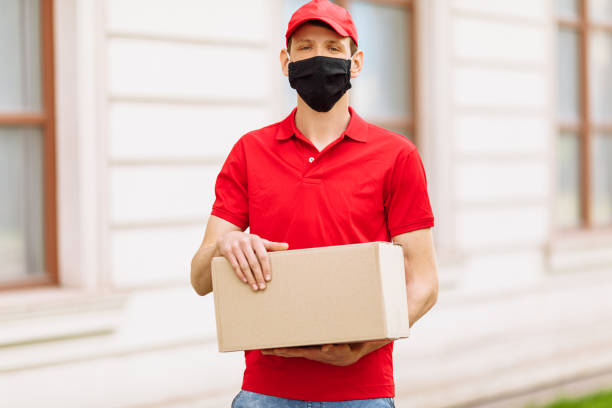 istock A courier employee in uniform and a protective face mask holds an empty cardboard box outdoors 1227146451