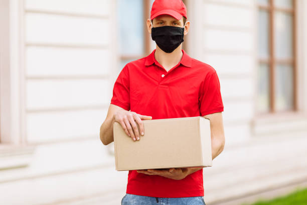 istock A courier employee in uniform and a protective face mask holds an empty cardboard box outdoors 1227147514