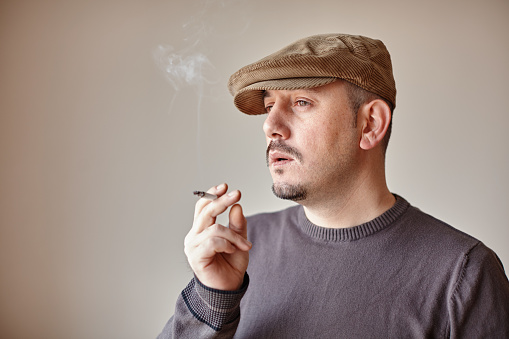 Portrait of a caucasian man with a hat taking a smoke from his cigarette