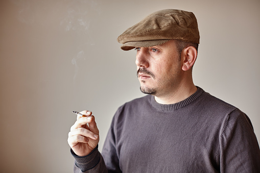 Portrait of a caucasian man wearing a hat looking away with a suspicious expression while smoking a cigarette