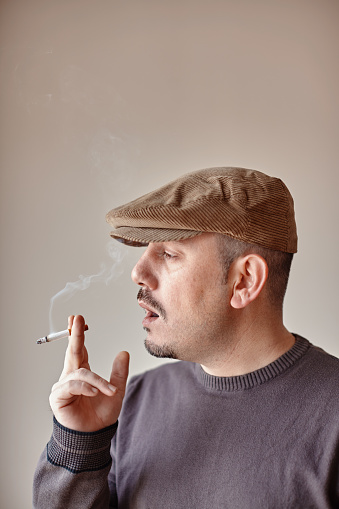 Portrait of a caucasian man with a hat taking a smoke from his cigarette