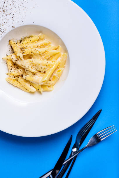 Pasta penne with cheese and creamy sauce in white plate on bluevbackground.
