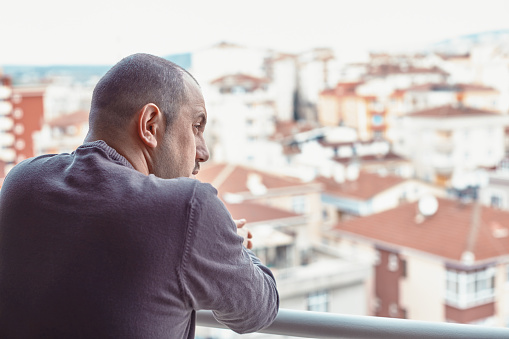 Rear view of a man standing on the balcony and looking over the city