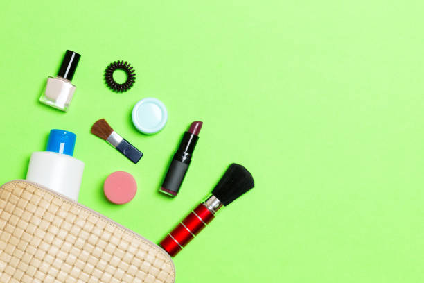 aerial view of a leather cosmetics bag with make up beauty products spilling out on green background. beautiful skin concept with copy space - pampering nail polish make up spilling imagens e fotografias de stock