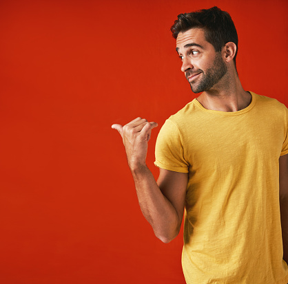 Studio shot of a handsome young man pointing against a red background