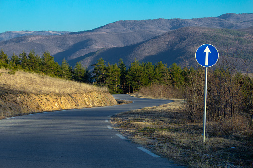 A curvy road with a go straight ahead sign on a rural road in Bulgaria