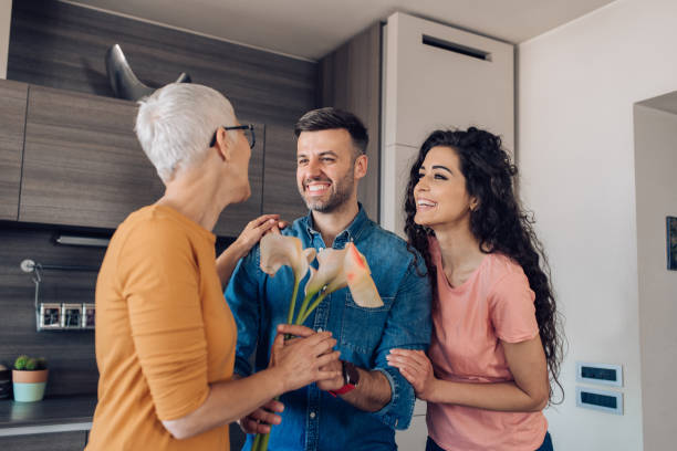 Senior woman getting a flower bouquet from her son and daughter-in-law Man and his wife giving flowers to his mother for Mother's day. mother in law stock pictures, royalty-free photos & images