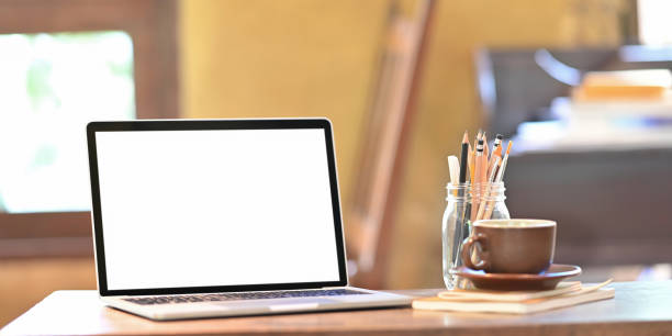 istock Computer laptop putting on wooden working desk that surrounded by ceramic coffee cup and pencils in glass vase over orderly sitting room as background. 1227154518