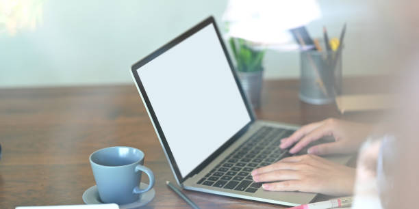 istock Cropped image of beautiful woman typing on white blank screen computer laptop that putting on wooden working desk surrounded by potted plant, pencil holder and coffee cup. 1227155157