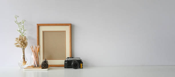 istock Camera with lens putting on photographer desk that surrounded by pine cone, stack of notebook, empty picture frame, pencils in glass vase and wild grass in bottle. 1227155283