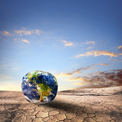 Conceptual climate change image of deformed World on dry and cracked landscape over clear sky.\nNasa image used:\nhttps://apod.nasa.gov/apod/image/0304/bluemarble2k_big.jpg