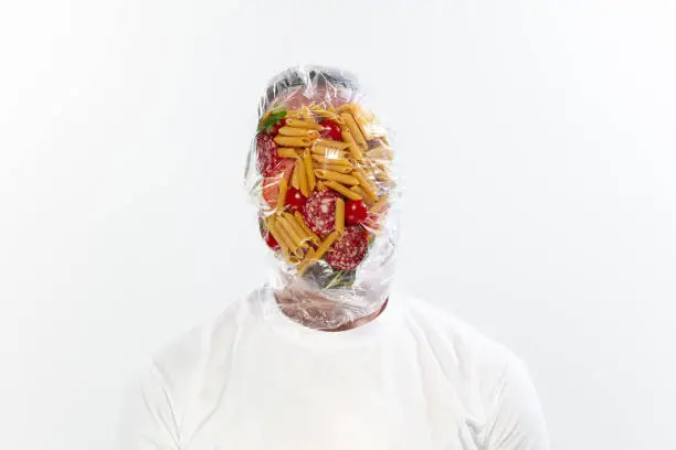 Photo of Male face covered with oilcloth, cellophane and unhealthy food, hard to breathe. People lost their faces, can't notice the environmental pollution made by themself.
