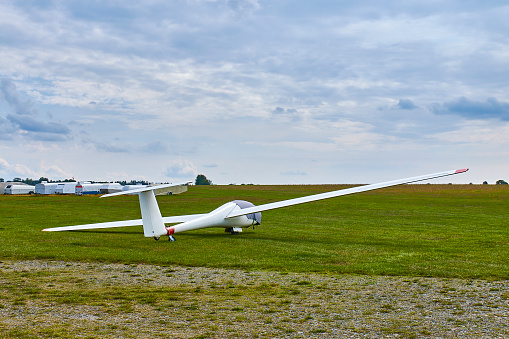 Glider plane standing on grass airport runway with dramatic sky background.