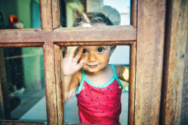 Close up of baby girl standing and looking through the window