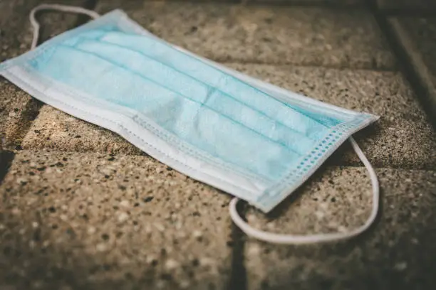 Close-up of a disposable surgical mask used as protection against Coronavirus or Covid-19 infection thrown on the street in the sunlight