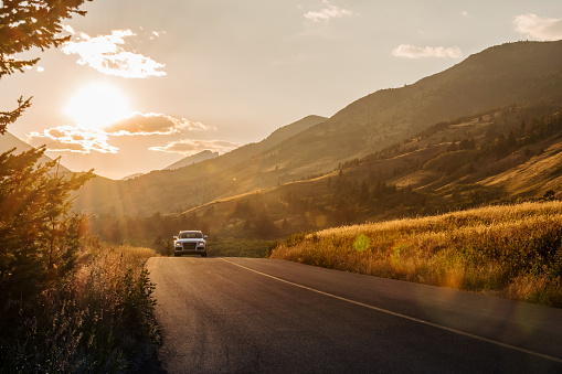 A white car drives down a curving road through Waterton Lakes National Park on the way back from Red Rock Canyon. Sun rays are lighting up smoke from forest fires in August 2017.