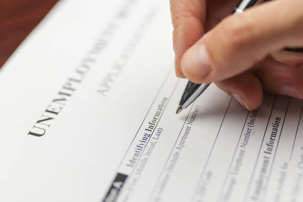 Close-up of a person's hand filing social security benefits application form.  Concept of coronavirus and stay at home order impact on economy. Selective focus, extremely shallow DOF.