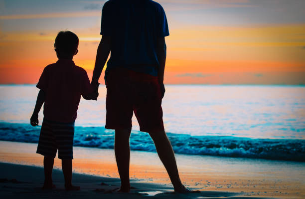 夕日の海で手をつないでいる父と息子のシルエット - trust human hand sea of hands holding ストックフォトと画像