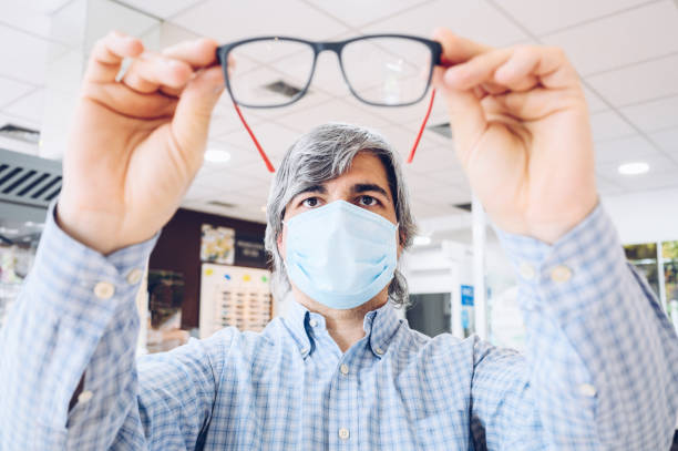 Middle-aged man wearing flu mask holding modern glasses in his hands