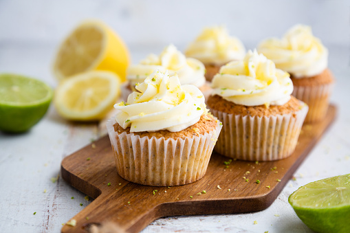 Lemon and poppy seed cupcakes with cheese cream frosting and lemon and lime zest on a cutting board