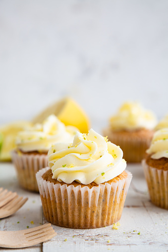 Lemon and poppy seed cupcakes with cheese cream frosting and lemon and lime zest on a rustic white wooden table