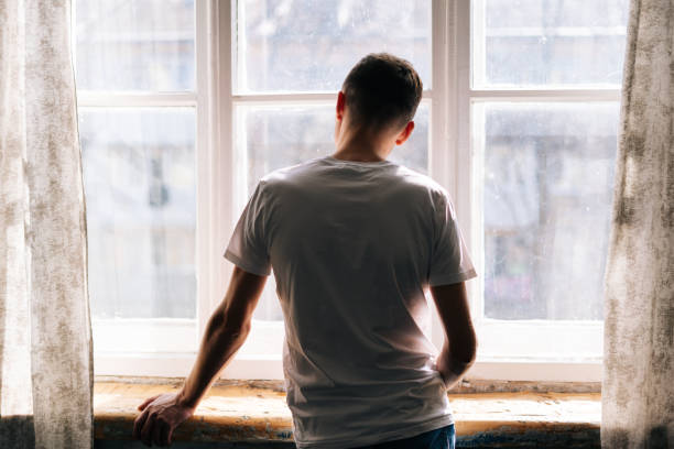 un joven irreconocible se para junto a la ventana en el día soleado. - window sun sunlight vertical fotografías e imágenes de stock