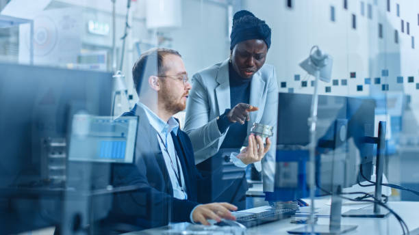 istock Modern Factory: Female Project Supervisor Talks to a Male Industrial Engineer who Works on Computer. They Inspect Machinery Mechanism and Design Improved Version. Working High-Tech Industrial Facility 1227179654