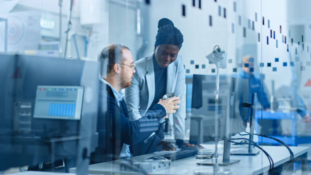 istock Modern Factory: Female Project Supervisor Talks to a Male Industrial Engineer who Works on Computer. They Inspect Machinery Mechanism and Design Improved Version. Working High-Tech Industrial Facility 1227179666