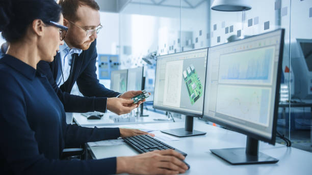 istock Modern Electronics Factory: Male Supervisor Talks to a Female Electrical Engineer who Works on Computer with CAD Software. Developing PCB, Microchips, Semiconductors and Telecommunications Equipment 1227179690