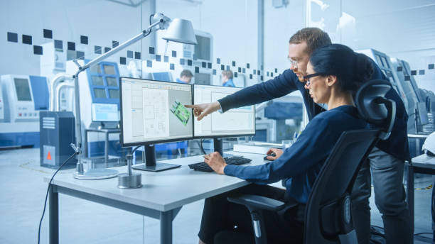 istock Modern Electronics Factory: Male Supervisor Talks to a Female Electrical Engineer who Works on Computer with CAD Software. Developing PCB, Microchips, Semiconductors and Telecommunications Equipment 1227179696