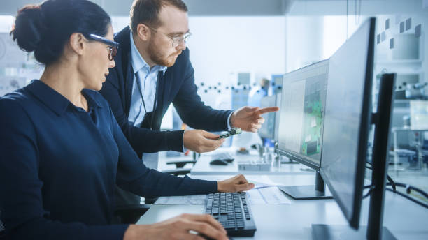 istock Modern Electronics Factory: Male Supervisor Talks to a Female Electrical Engineer who Works on Computer with CAD Software. Developing PCB, Microchips, Semiconductors and Telecommunications Equipment 1227179713