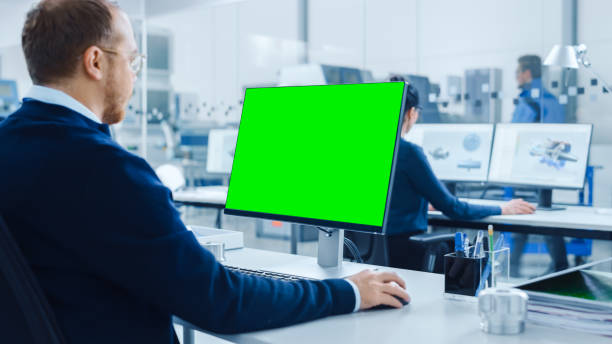istock Over the Shoulder: Heavy Industry Engineer Working on Personal Computer, Display is Green Mock-up Screen or Chroma Key. Industrial Factory with High-Tech CNC Machinery 1227179774