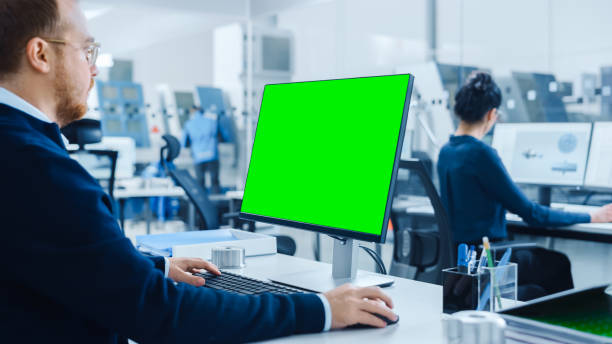 istock Over the Shoulder: Heavy Industry Engineer Working on Personal Computer, Display is Green Mock-up Screen or Chroma Key. Industrial Factory with High-Tech CNC Machinery, Professionals Working 1227179790