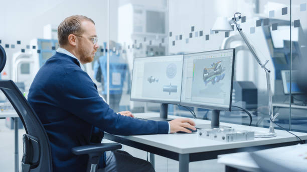 istock Male Industrial Engineer Solving Problems, Working on a Personal Computer, Two Monitor Screens Show CAD Software with 3D Prototype of Hybrid Electric Engine Being Tested. Working Modern Factory 1227179833