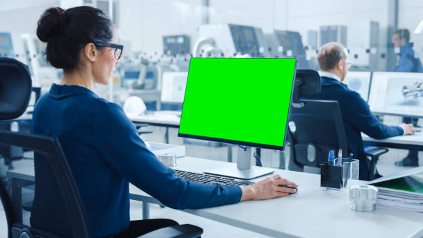 istock Over the Shoulder: Female Chief Engineer Working on Personal Computer, Display is Green Mock-up Screen or Chroma Key. Industrial Factory with High-Tech Machinery and Professional Workers 1227179855