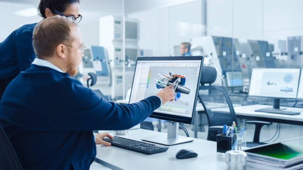 istock Modern Factory: Female Project Supervisor Talks to a Male Industrial Engineer who Works on Personal Computer. They use CAD Software for Design and Development of Hybrid Hydrogen Engine Prototype 1227179858