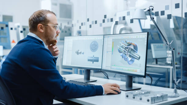 istock Male Industrial Engineer Solving Problems, Working on a Personal Computer, Two Monitor Screens Show CAD Software with 3D Prototype of Hybrid Electric Engine Being Tested. Working Modern Factory 1227179906