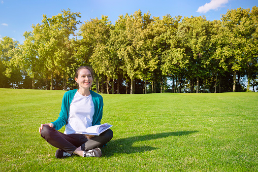 Young smiling woman on the lawn with a book in her hands.