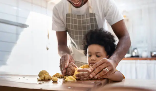 Photo of Black family having fun prepare bakery together at home. African American father and adorable son kneading dough in kitchen. Happy loving Man and little helper boy enjoy while making cakes and cookies