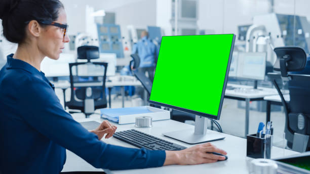 istock Over the Shoulder: Female Chief Engineer Working on Personal Computer, Display is Green Mock-up Screen or Chroma Key. Industrial Factory with High-Tech Machinery and Professional Workers 1227182128