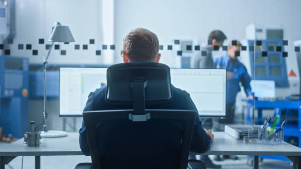istock Male Industrial Engineer Solving Problems, Working on a Personal Computer, Two Monitor Screens Show CAD Software with 3D Prototype of Zero-Emissions Engine Being Tested. Back View 1227182306