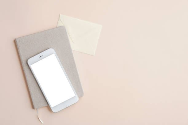 istock Flat lay, top view office desk table with mobile phone mockup with blank white screen, paper notebook and envelope on beige background. Business and technology concept. 1227182388