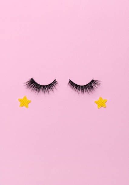 istock Creative layout with eyelashes. Closed eyes on pastel pink background 1227191595