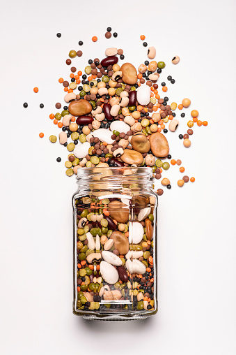 glass jar with a large variety of dried legumes in the foreground, top view, isolated from the white background
