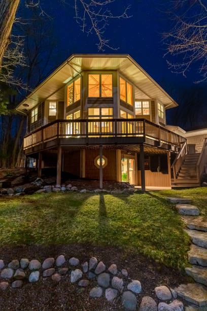 Luxury Home in the Woods at Night Luxury home with illuminated windows and a large composite deck in the woods.  Photographed at night.  Concepts could include architecture, design, outdoor living, luxury living, nature, others. real estate outdoors vertical usa stock pictures, royalty-free photos & images