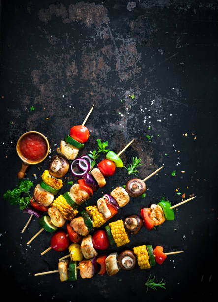 Chicken kebabs on skewers with mushrooms and vegetables Chicken kebabs on skewers with mushrooms and vegetables on dark background shish kebab stock pictures, royalty-free photos & images